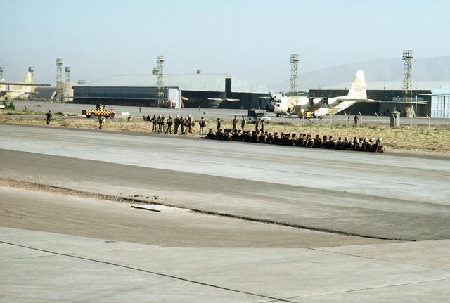 Iranian paratroopers wait at Shiraz Air Base to board a C-130 Hercules aircraft (background) for a training mission during Exercise CENTO. (August 1, 1977)