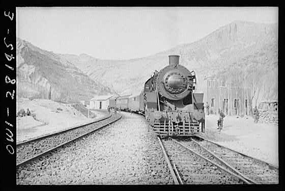 Somewhere in Iran. An American engine transporting allied aid for Russia, stopping at a station rimmed by mountains.
