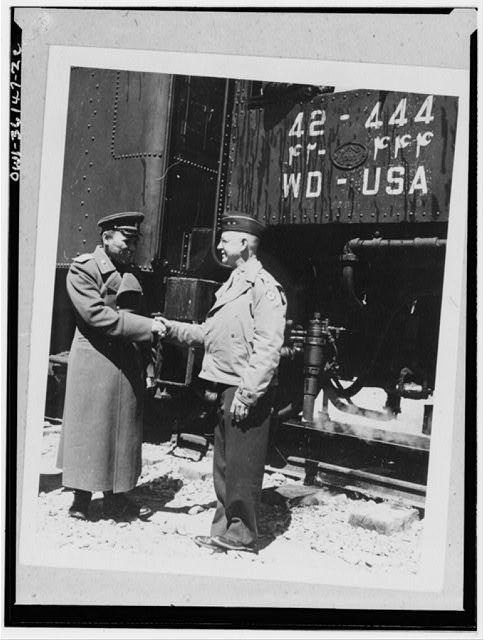Against a background of an American locomotive inscribed with English and Persian numerals, Major-General Donald H. Connolly, Commanding Gerneral, Persian Gulf Service Command exchanging greetings with General A.M. Koroloff on the occasion of the arrival of the first All-American train from the Persian Gulf to the point where the freight load was turned over to the USSR (Union of Soviet Socialist Republics).
